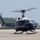 A dark navy blue and white United States of America government helicopter is captured on a tarmac, appearing to be in the process of landing or taking off. The aircraft bears the inscription 'United States of America' along its fuselage and displays an American flag near the rotor assembly. The rotor blades are visibly in motion, shown by motion blur, indicating active operation.