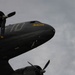 A dark olive/black painted WWII-era C-47 Skytrain transport aircraft photographed from a low angle against an overcast sky. The aircraft bears the nose art name 'Placid Cassie' in yellow lettering and the number '10' on its fuselage. A second aircraft, partially visible in the lower frame, bears the name 'Lady Eileen' near its engine cowling.