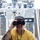 Forged Underwater: PNSY Dive Team Conducts Inspection of New Caisson A tattooed man wearing a Patagonia cap and a yellow 'Jetty' branded t-shirt is looking through binoculars aboard what appears to be a vessel's bridge or helm station. Behind him is a large stainless steel ship's wheel and an extensive panel of navigation and control equipment. The image is sharp and well-lit, capturing a nautical observation scene.