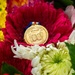 A gold National Guard Retirement medal rests on a vibrant red gerbera daisy surrounded by a colorful floral arrangement. The medal features engraved text reading 'NATIONAL GUARD' and 'RETIREMENT' with decorative imagery, suspended from a red, white, and blue ribbon. The composition suggests a retirement ceremony or commemorative occasion honoring military service.