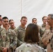 A group of U.S. Air Force personnel in OCP (Operational Camouflage Pattern) uniforms are gathered inside what appears to be a tent or temporary structure. A senior military officer in a tan/desert flight suit is addressing or conversing with the assembled airmen. The setting suggests a briefing, visit, or informal meeting at a forward operating location.