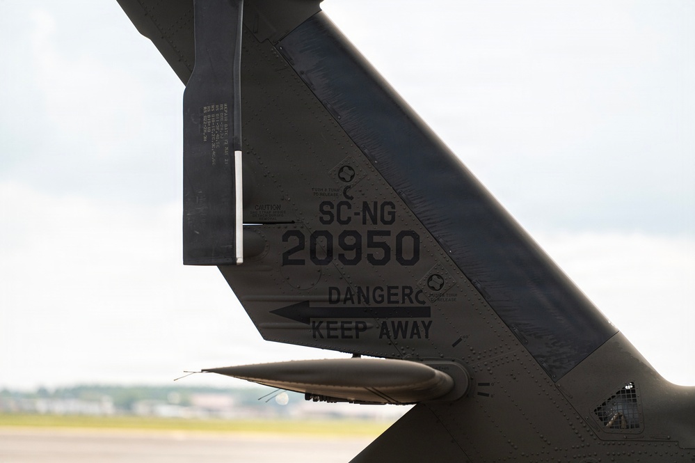 Close-up photograph of the tail section of a military aircraft marked with the identifier 'SC-NG 20950', indicating it belongs to the South Carolina National Guard. The dark olive/black painted surface displays safety markings including a 'DANGER KEEP AWAY' warning with a directional arrow. The image was taken on an airfield tarmac under overcast skies.