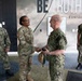 Four military personnel are gathered in front of a building entrance featuring a 'BE TRUTHFUL' quote attributed to Edward R. Murrow. A U.S. Army soldier in OCP (Operational Camouflage Pattern) uniform is shaking hands with a senior U.S. Navy officer in NWU Type III uniform, suggesting a formal greeting or meeting. Two additional Navy personnel in NWU Type III uniforms are present, one on each side.