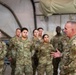 A senior military officer in OCP (Operational Camouflage Pattern) uniform is addressing a group of approximately 20 military personnel inside what appears to be a large military tent or temporary structure. The speaker, positioned on the right side of the frame, is gesturing with his hands while speaking to the assembled troops who are standing at ease. The setting suggests a briefing, commander's call, or unit address at a forward operating location.