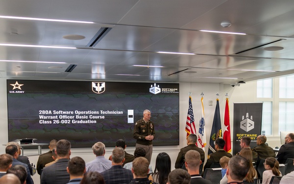 A U.S. Army graduation ceremony for the 280A Software Operations Technician Warrant Officer Basic Course, Class 26-002, is taking place at the Army Software Factory. A uniformed officer stands at the front of the room addressing an audience of approximately 40-50 attendees seated in rows. The event is held in a modern facility with branded 'Software Factory' signage and military flags displayed prominently.