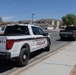 A Marine Corps Police Ford F-150 pickup truck is parked or slowly moving along a residential street in what appears to be a desert Southwest location, likely a military base housing area. The vehicle is marked with '911' and 'Marine Corps Police' insignia with red and gold striping. A second dark-colored pickup truck is visible ahead on the same street.