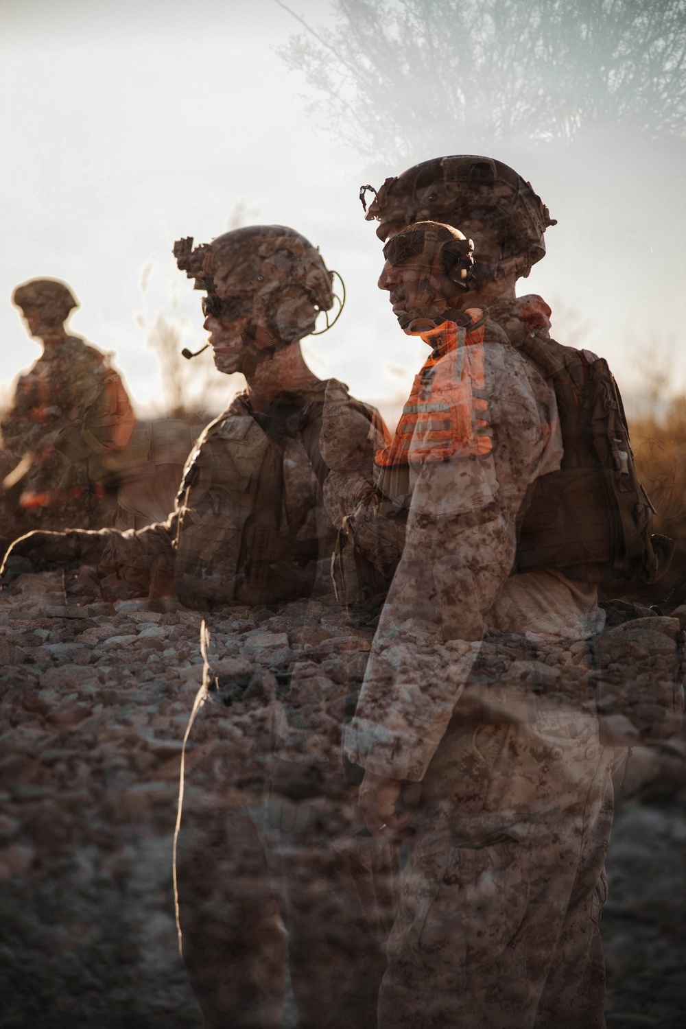 A double-exposure or composite photograph showing military personnel in full tactical gear in an arid outdoor environment. At least three soldiers are visible wearing combat helmets, body armor, and communication headsets. The layered photographic technique creates a ghostly, semi-transparent effect overlapping multiple exposures of the same or different subjects.