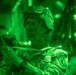 A night-vision photograph showing a military soldier wearing combat gear and a patrol cap inside what appears to be a military aircraft. The image is captured entirely in the characteristic green monochrome of night-vision optics. A shoulder patch is visible on the soldier's uniform, appearing to read 'Ranger' and 'Airborne'.