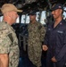 Three U.S. Navy personnel are engaged in conversation aboard what appears to be the bridge of a naval vessel. Two sailors are in Navy Working Uniform (NWU) camouflage pattern while one is in navy blue coveralls. The setting is clearly a ship's bridge with navigation equipment and windows visible in the background.