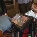 A gloved hand operates a Foster+Freeman forensic imaging device, specifically a Crime-lite AUTO unit mounted on a tripod. The tablet display shows what appears to be a forensic examination in progress, likely fingerprint or trace evidence analysis under specialized lighting. Several individuals are visible in the background observing the procedure.