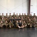 A large group of military personnel posed for a formal group photo inside what appears to be a training facility or gymnasium. The majority are wearing Army Combat Uniforms (ACU/OCP pattern), while several individuals on the edges wear black 'MACP' branded athletic shirts. They are gathered around a banner reading 'MACP - Modern Army Combatives - Pennsylvania [unit] Combatives.'