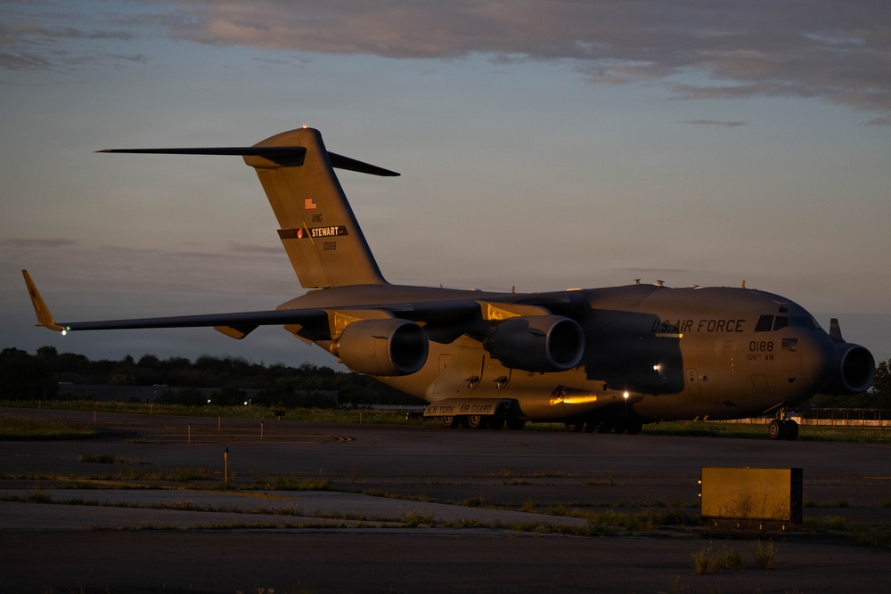 A U.S. Air Force C-17 Globemaster III military cargo aircraft is parked on a tarmac at dusk or dawn. The aircraft belongs to the New York Air National Guard, based at Stewart Air National Guard Base, with tail number 0188. The warm golden light of the low sun illuminates the aircraft against a partly cloudy sky.