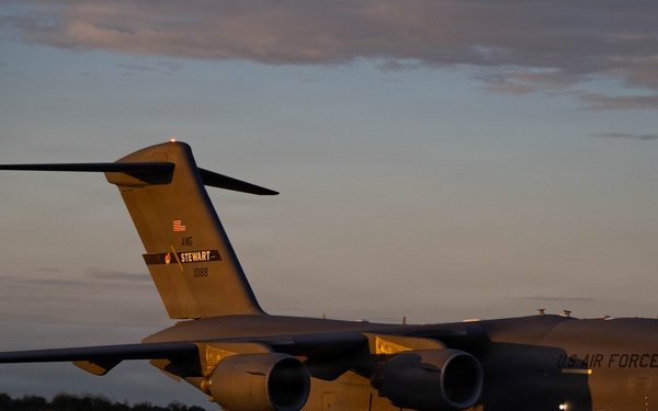 A U.S. Air Force C-17 Globemaster III military cargo aircraft is parked on a tarmac at dusk or dawn. The aircraft belongs to the New York Air National Guard, based at Stewart Air National Guard Base, with tail number 0188. The warm golden light of the low sun illuminates the aircraft against a partly cloudy sky.