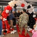 A grand opening or ribbon-cutting ceremony for a Black Rifle Coffee Company location, featuring a decorative balloon arch in red, white, and black colors over a red carpet entrance. Military personnel in camouflage uniforms are present alongside civilians, with handshakes being exchanged near the entrance. The event appears festive and celebratory with scattered balloons on the floor.