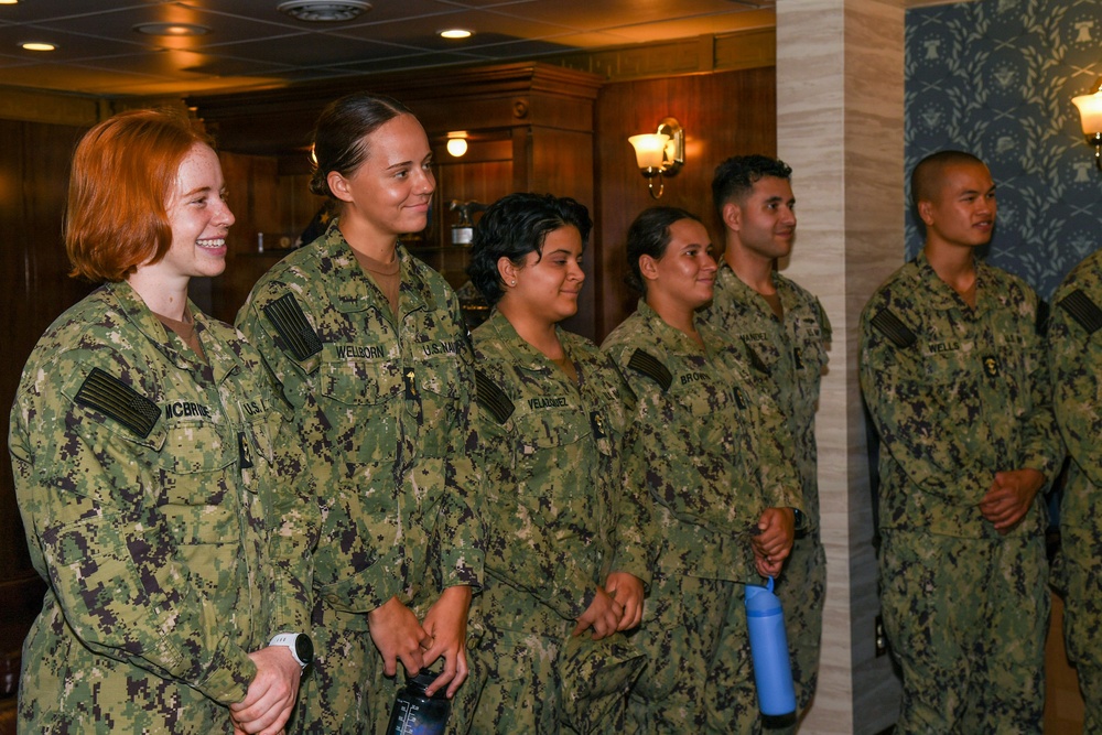 Six U.S. Navy personnel in NWU Type III (woodland digital camouflage) uniforms are standing in a line inside what appears to be a formal indoor military facility. The group consists of four women and two men, all appearing relaxed and smiling, suggesting a ceremonial or recognition event. Name tapes visible include McBride, Wellborn, Velasquez, Brown, Ramirez, and Wells.
