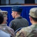 The image shows a group of military personnel at what appears to be a formal military event or ceremony. The central figure is a U.S. Air Force Colonel, identifiable by the silver eagle insignia on his flight cap and a unit patch on his flight suit. Surrounding personnel are wearing Army Combat Uniforms (ACU/OCP pattern), suggesting a joint-service gathering.
