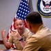 Two U.S. Navy officers in tan service uniforms are seated at a conference table engaged in discussion. The officer facing the camera is gesturing with both hands while speaking, with multiple service ribbons and a warfare device visible on his uniform. The setting is an official Navy office, indicated by the U.S. flag and a 'Chief of Naval Personnel' seal on the wall behind them.