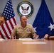 Three United States Navy personnel are seated at a conference table in what appears to be an official meeting setting. The central figure, a senior officer with multiple service ribbons and insignia, appears to be speaking or briefing the others. The setting is formal, backed by the U.S. flag, a Navy flag with a star, and the official seal of the United States Navy Chief of Naval Personnel.