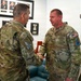 Two U.S. Space Force personnel in OCP (Operational Camouflage Pattern) uniforms are shaking hands in what appears to be an office or reception area. A scale model of Blue Origin's New Glenn rocket is prominently displayed to the right. The setting suggests an official military visit or recognition ceremony.