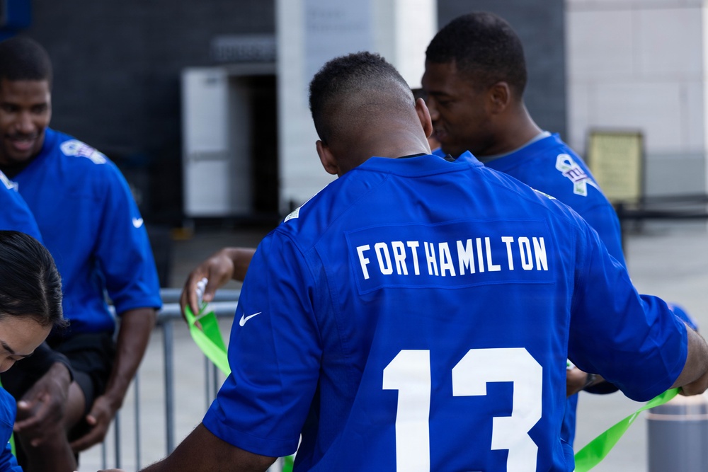 The image shows a group of young men wearing blue Nike football jerseys outdoors. The central figure is wearing jersey number 13 with 'FORTHAMILTON' printed on the back. The group appears to be engaged in some kind of team activity involving green ribbon or flag material.