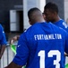 The image shows a group of young men wearing blue Nike football jerseys outdoors. The central figure is wearing jersey number 13 with 'FORTHAMILTON' printed on the back. The group appears to be engaged in some kind of team activity involving green ribbon or flag material.