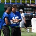Several players wearing New York Giants blue NFL jerseys are gathered on a sideline or practice field. The player wearing jersey number 15 appears to be reviewing a wristband playbook or electronic device with a teammate. Green flag football belts are visible, suggesting this may be a flag football or non-contact practice session.