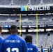 Four individuals wearing blue jerseys with 'FORTHAMILTON' printed on the back are standing on the field at MetLife Stadium, facing the field. The stadium appears largely empty, suggesting this is a pre-game or special event visit. The scoreboard displays '3rd &amp; 7' and a game clock reading '68:51'.