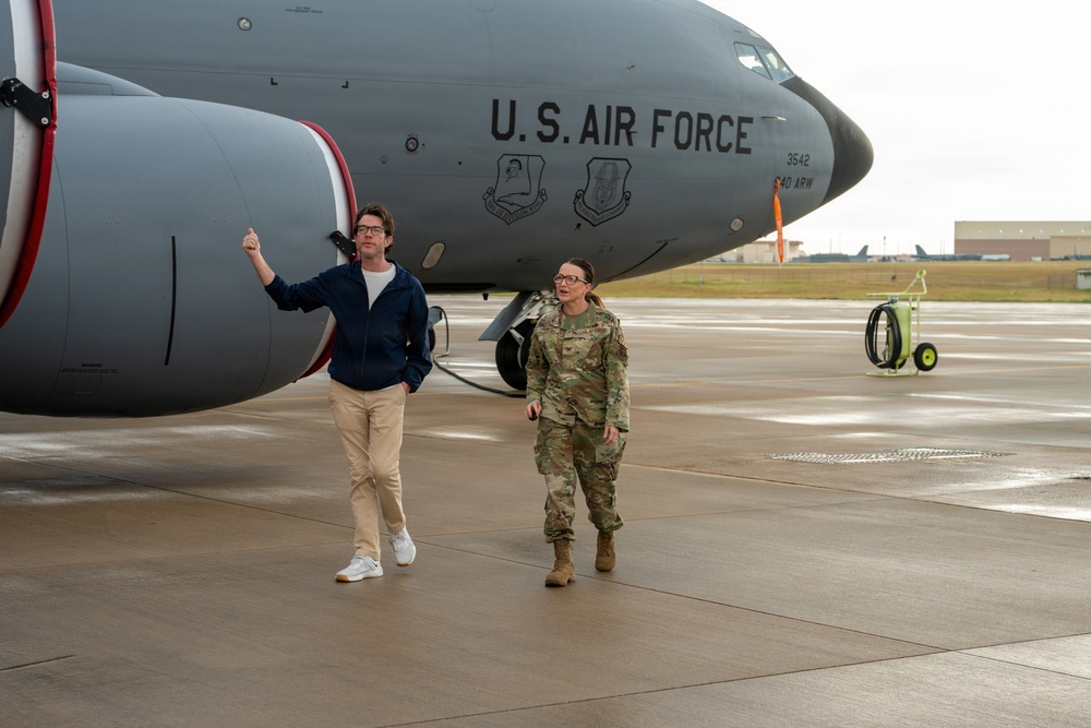 Two individuals stand on a military flight line in front of a U.S. Air Force aircraft, tail number 3542, bearing unit insignia and the marking '940 ARW' (Air Refueling Wing). One person is in civilian attire (blue hoodie, khaki pants, white sneakers) gesturing with a thumbs-up, while the other is in U.S. Air Force OCP (Operational Camouflage Pattern) uniform. The setting appears to be an active airfield tarmac, likely during a base visit or tour.