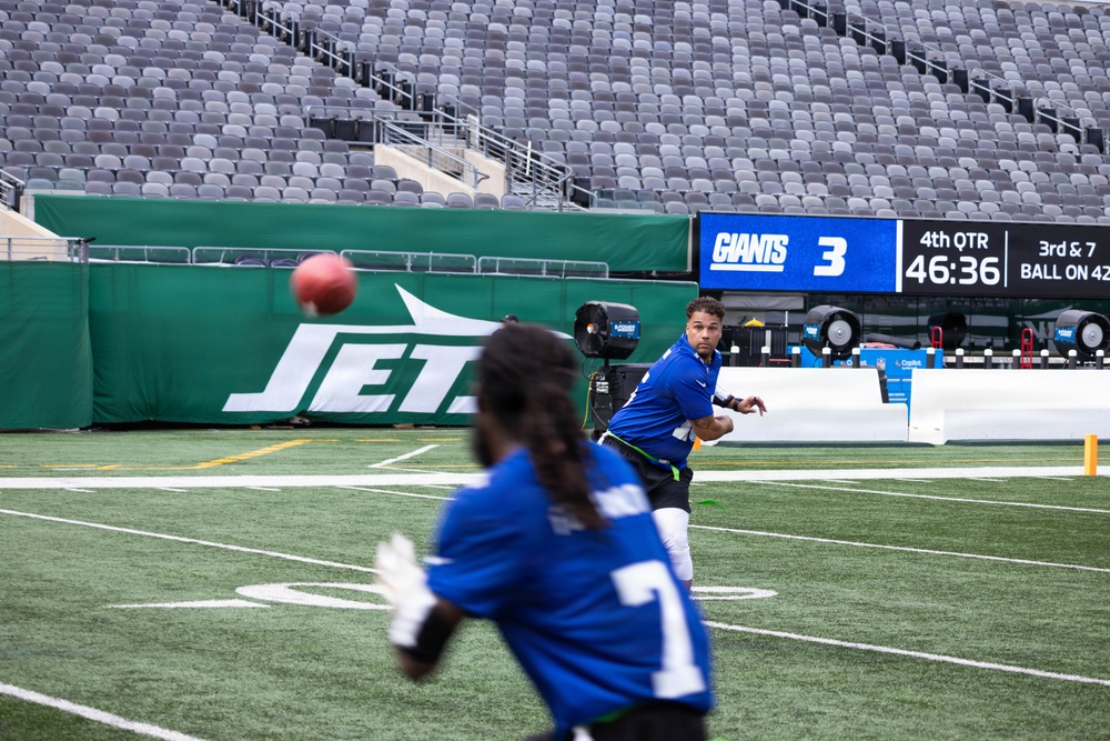 Two players in blue New York Giants uniforms are on the field at MetLife Stadium, with one player throwing a football to another. The scoreboard in the background shows the Giants with 3 points in the 4th quarter, 46:36 remaining, on a 3rd and 7 situation with the ball on the 42. The stadium seats are empty, suggesting this is a pre-game warmup or practice session.