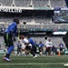 A flag football game is being played on the field at MetLife Stadium, home of the New York Giants and Jets. Players in blue and white/green uniforms are actively competing on the turf while spectators and staff watch from the sidelines. The stadium scoreboard shows a 4th quarter game situation with 0:29 remaining.