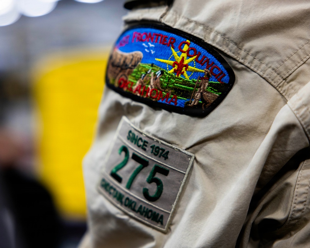 A close-up photograph of a Boy Scout uniform sleeve displaying two patches. The upper patch identifies the 'Last Frontier Council, Oklahoma' council patch with an embroidered scene. The lower patch identifies Troop 275, based in Checotah, Oklahoma, established since 1974.