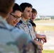 A group of young teenagers, several wearing Boy Scouts of America (BSA) uniforms, are standing at a railing overlooking what appears to be an airport tarmac or airfield. The scouts appear to be on an organized field trip or educational visit, observing aircraft operations from an elevated observation area. The image is taken during golden hour lighting, giving it a warm tone.