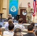 A U.S. military officer in camouflage uniform is addressing an audience in a conference or briefing room setting. The speaker stands near a podium beside a U.S. flag and a banner reading 'Building Peace Through Strength' with the text 'Connect' and 'Empower' visible. The audience, seated in rows of chairs, appears to include both military and civilian attendees, several wearing Hawaiian-style shirts.