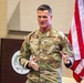 A U.S. Air Force officer wearing OCP (Operational Camouflage Pattern) uniform with the name tape 'CROWLEY' and a one-star general rank insignia is speaking at what appears to be an official military briefing or presentation. He is gesturing with both hands, suggesting active engagement with an audience. An American flag and what appears to be an official seal or emblem are visible in the background.