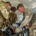 Three U.S. Army soldiers in OCP (Operational Camouflage Pattern) uniforms are providing medical treatment to a patient lying on a military litter inside a field tent. The personnel, identifiable by name tapes 'SIDES' and 'RAMIREZ', are performing what appears to be a medical assessment including blood pressure measurement and airway management. This appears to be either a field training exercise or an actual forward medical treatment scenario.