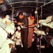 The image shows the interior of a military medical evacuation aircraft filled with litter patients on stacked stretchers along both sides of the fuselage. Two standing personnel in military-style clothing appear to be reviewing or completing paperwork/clipboards, while a third person in white attire is seated nearby. The scene is consistent with aeromedical evacuation operations, likely from the Vietnam War era based on photo quality, clothing, and aircraft interior design.