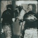 A black-and-white/sepia-toned photograph showing military personnel engaged in a boxing or martial arts training session. One individual wearing an Everlast boxing headgear and gloves appears to be sparring or drilling, while others in USMC digital camouflage (MARPAT) uniforms observe or participate. The setting appears to be an indoor training space, possibly a forward operating base or military facility.