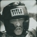 A black-and-white photograph of a U.S. Marine wearing a 'Title Boxing' headgear and digital camouflage (MARPAT) uniform. The individual's name tape reads 'LAGUNES' and the branch tape reads 'U.S. MARINES.' The subject appears to be engaged in a boxing or combatives training session.