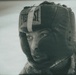 A close-up portrait of a person wearing an Everlast brand boxing headguard. The image has a vintage, grainy film aesthetic with a muted, desaturated tone. The subject appears focused and is wearing what looks like a camouflage or patterned garment.