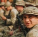 A young soldier in the foreground is looking back over his shoulder toward the camera with a slight smile. He is wearing MultiCam (OCP) pattern camouflage uniform and a boonie hat. Behind him, several other soldiers in similar uniforms are visible but out of focus.
