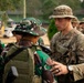 The image shows a multinational military exercise or joint training event involving U.S. Army soldiers and what appear to be Indonesian Armed Forces (TNI) personnel, identifiable by their distinctive green camouflage uniforms and boonie hats. A U.S. soldier wearing a '4th Infantry Division' patch and 'U.S.' chest tape is interacting with foreign military counterparts, possibly reviewing equipment or conducting a briefing. Additional personnel in Australian-style camouflage are visible in the background.