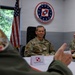 A military meeting or briefing is taking place at a facility associated with the 52nd Operations Group Detachment 1, as indicated by the unit insignia on the wall. A name placard identifies 'Brig Gen Chojnacki' at the conference table, suggesting a bilateral or multinational military engagement. An American flag is visible in the background alongside the unit patch bearing the motto 'Razem Silniejsi' (Polish for 'Stronger Together').