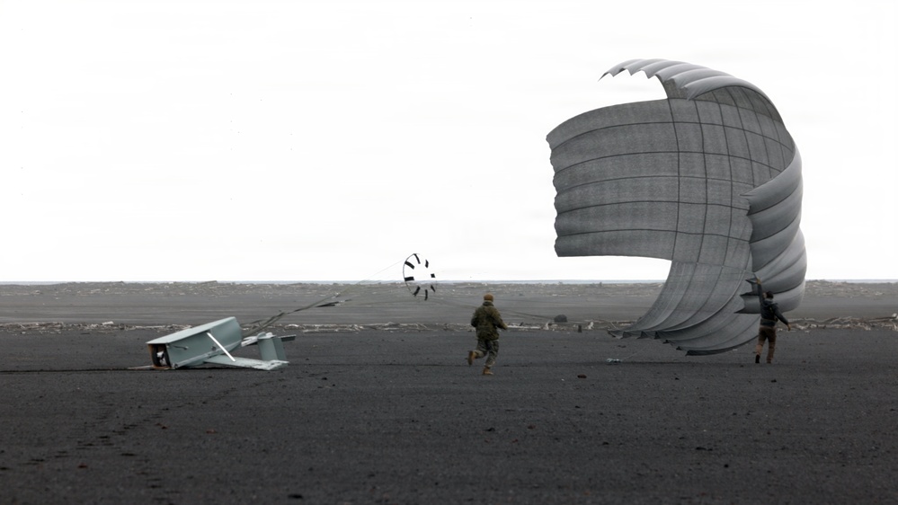 Two individuals are on a dark, flat terrain attempting to manage a large deployed parachute that is being inflated or dragged by wind. A piece of metal equipment or structure lies toppled on the ground to the left, and a smaller parachute or drogue chute is visible in the background. The overcast sky and dark ground suggest a remote, possibly coastal or volcanic landscape.