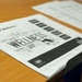 The image shows printed wellness-related documents laid open on a wooden desk. The main visible document features a word cloud design centered around the word 'WELLNESS' along with related terms. Additional papers are visible in the background, and handwritten notes appear on one of the documents.