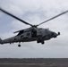A U.S. Navy MH-60R Seahawk helicopter marked '701' and assigned to HSM-46 is hovering low over what appears to be the flight deck of a naval vessel. The helicopter's main rotor blades are in motion, visible as a blur, indicating active flight operations. The image was taken from a low angle on the flight deck, with an overcast sky in the background.
