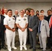 A formal group photo taken at a Navy Medicine facility, showing U.S. Navy personnel in white dress uniforms alongside civilians in business attire, including what appears to be a Japanese delegation. The setting features American and other flags in the background along with a 'Navy Medicine' seal/logo on the wall. The gathering suggests an official diplomatic or military-civilian exchange event.