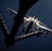 An aerial refueling operation is captured from the perspective of a tanker aircraft, showing a fighter jet approaching the refueling boom. The foreground displays the tanker's tail stabilizer with the word 'ALASKA' inscribed, while an F-16 Fighting Falcon closes in for fuel transfer. The image is dramatically lit with strong contrast, highlighting the fighter's airframe and weapons loadout against a dark background.