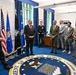 A group of approximately eight individuals are gathered in what appears to be a formal office within the Department of the Air Force, standing on a large official seal rug. The group includes civilians in business attire, one uniformed military officer in dress blues, and two individuals in Army combat uniforms. The atmosphere appears cordial and informal, with several people smiling and laughing.