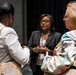 Three women are engaged in conversation at what appears to be a professional conference or event. The central figure, wearing a black blazer and conference lanyard, appears to be speaking to the other two attendees. The setting suggests a networking or post-session discussion in a conference venue.
