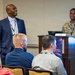 A U.S. Air Force service member in OCP (Operational Camouflage Pattern) uniform stands at a wooden podium labeled 'JVT2' during what appears to be a professional conference or briefing. A civilian in a dark blue suit stands beside him, both smiling toward an audience. The podium displays a graphic reading 'Digital Edge: [Edge] to Orbit,' suggesting a technology-focused military event.